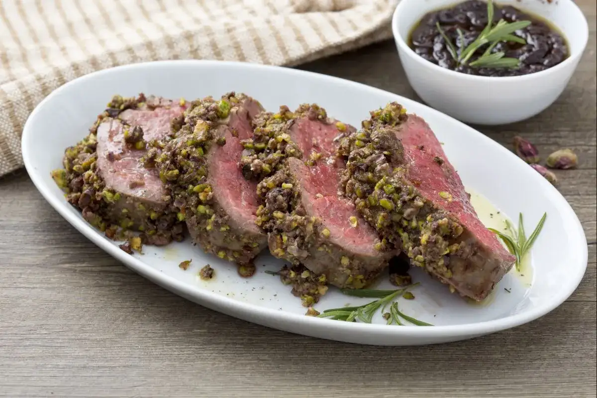 Tranches de filet mignon en croûte de pistaches et d'olives, servies avec une sauce foncée.