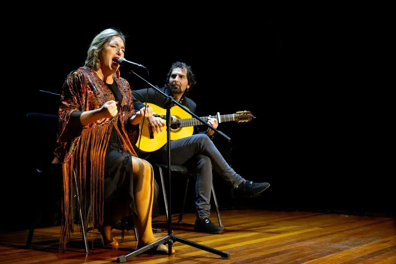 Una mujer canta apasionadamente mientras un hombre toca la guitarra, evocando la rica historia del flamenco.