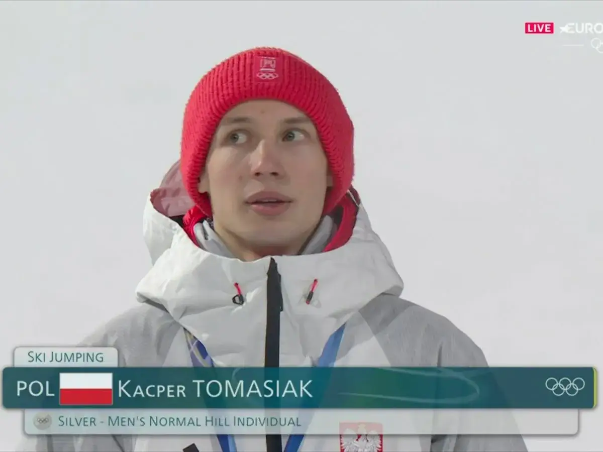 Kacper Tomasiak, polski skoczek narciarski, w czerwonej czapce i kurtce, z dumą reprezentuje swoich rodziców i Polskę.