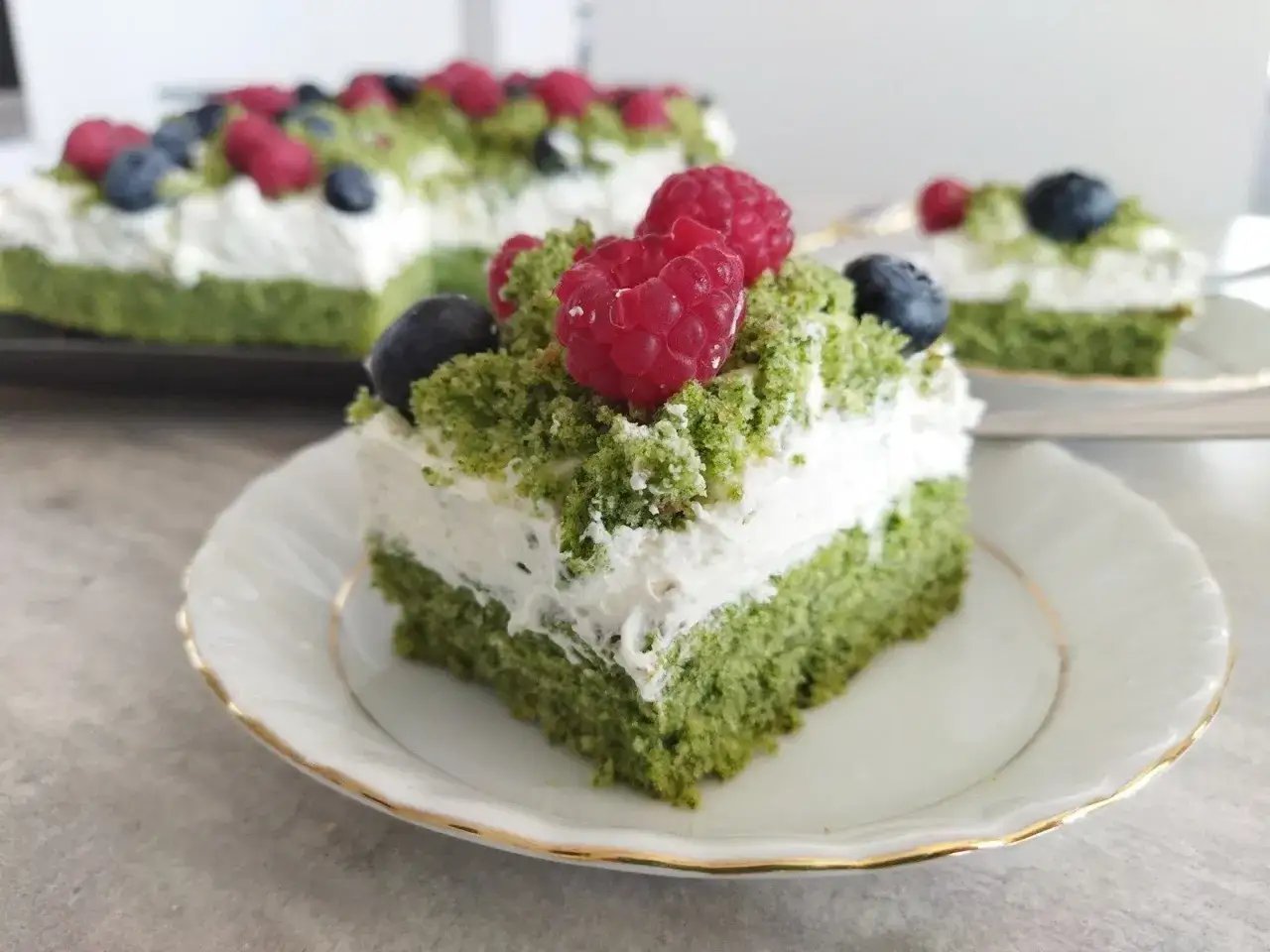 Pyszne ciasto zielony mech z malinami i borówkami, udekorowane kremem i zieloną posypką.