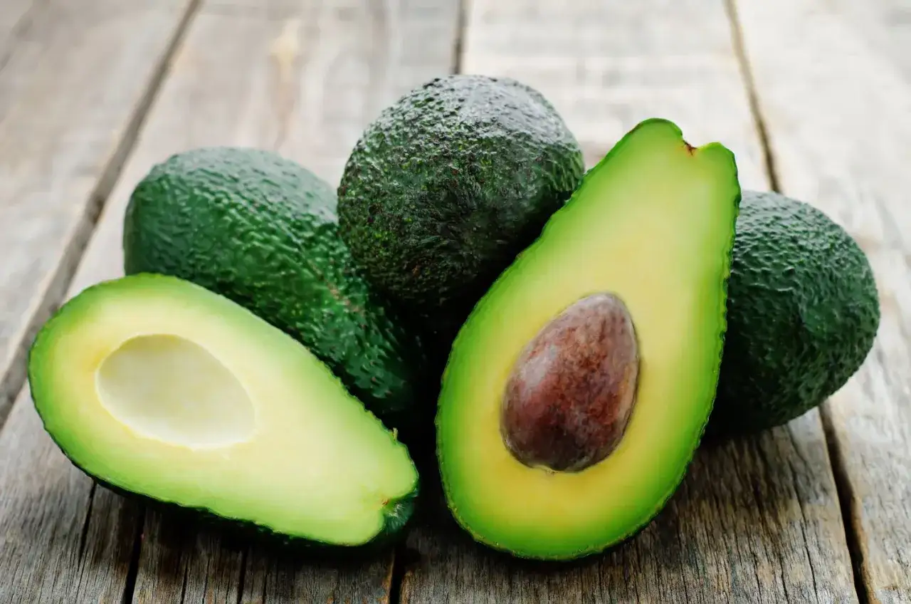 Frische Avocados, eine aufgeschnitten, liegen auf Holz. Tipps zum Avocado lagern.