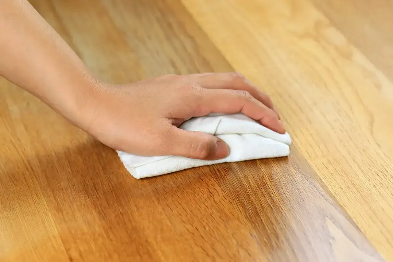Mano limpiando madera con paño blanco, mostrando cómo quitar manchas de la madera sin dañarla.