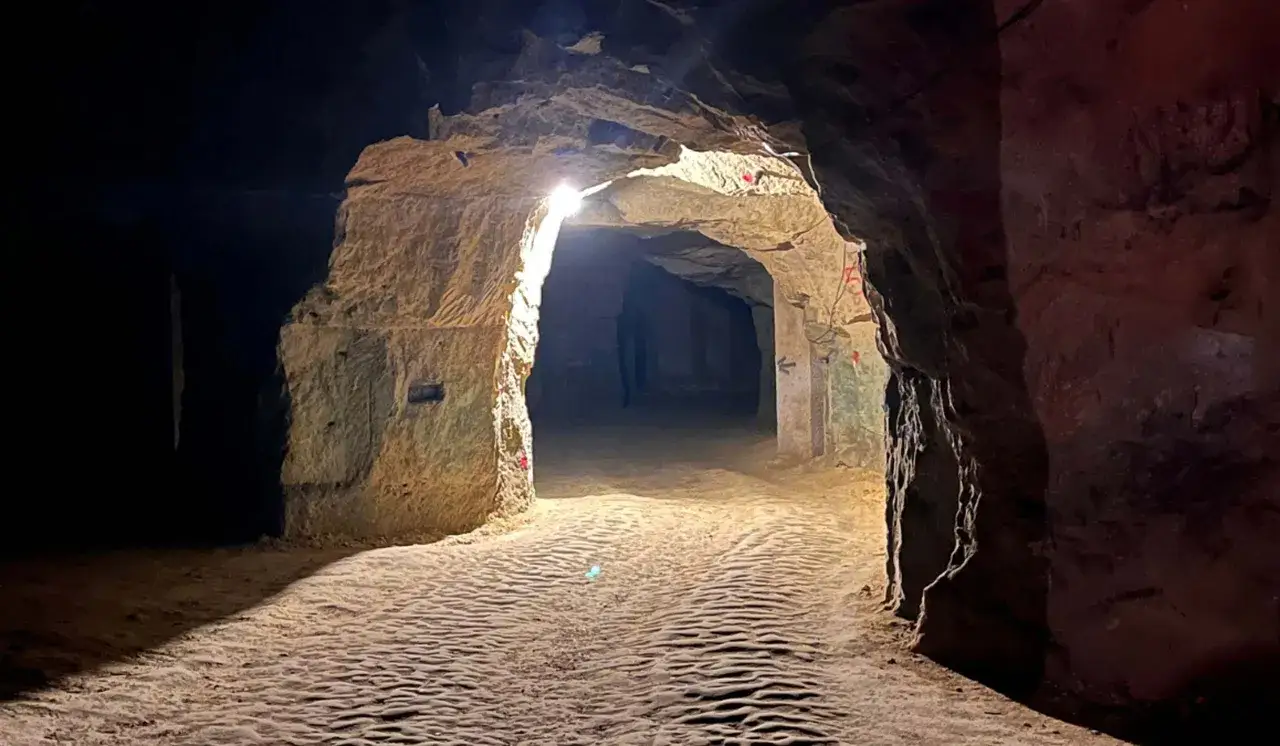 Un chemin s'enfonce dans une **cave troglodyte** éclairée par des lumières artificielles, révélant des parois rocheuses sculptées.
