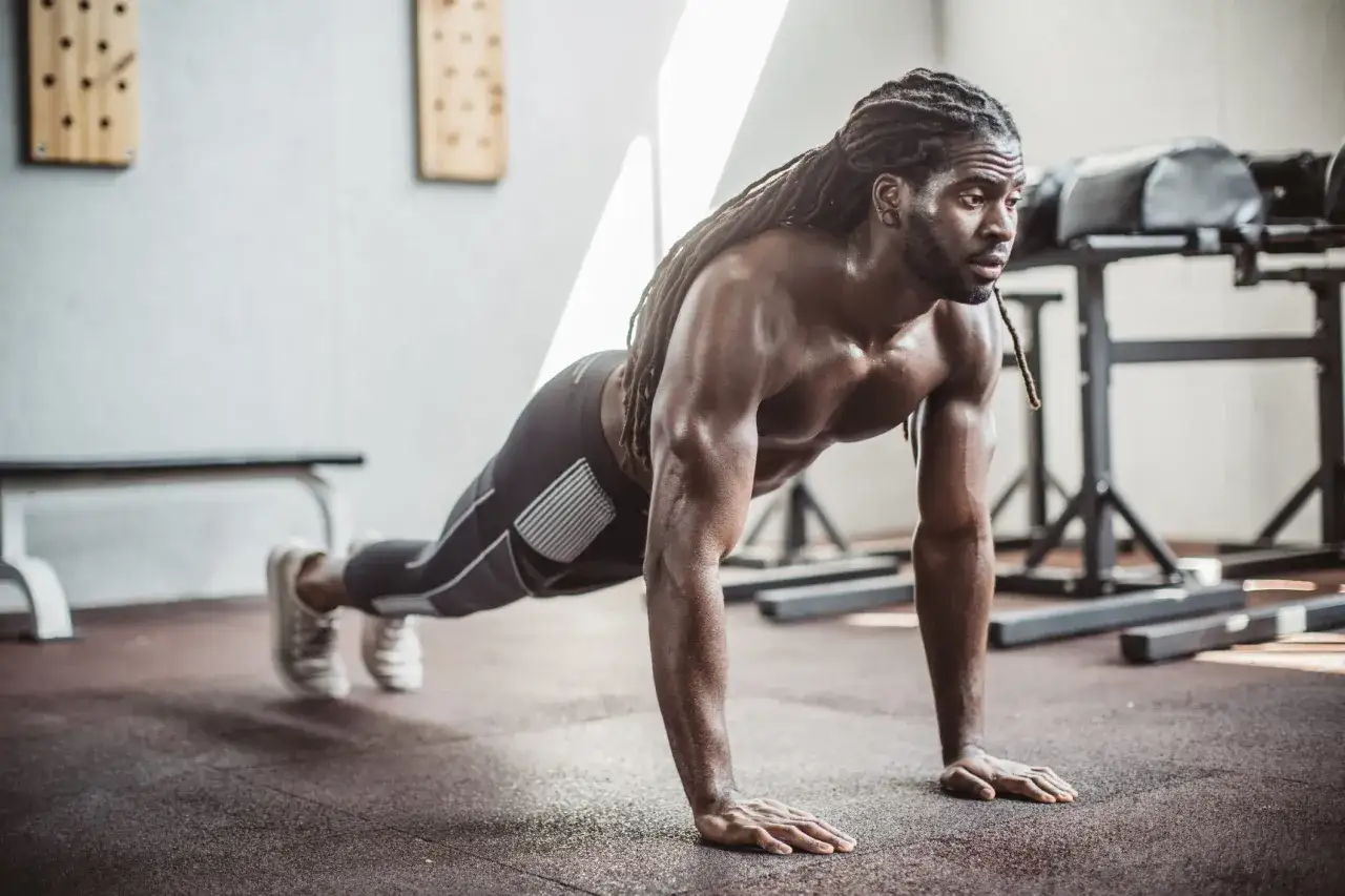 Un homme musclé en position de pompe, un exercice polyarticulaire essentiel pour le renforcement musculaire.