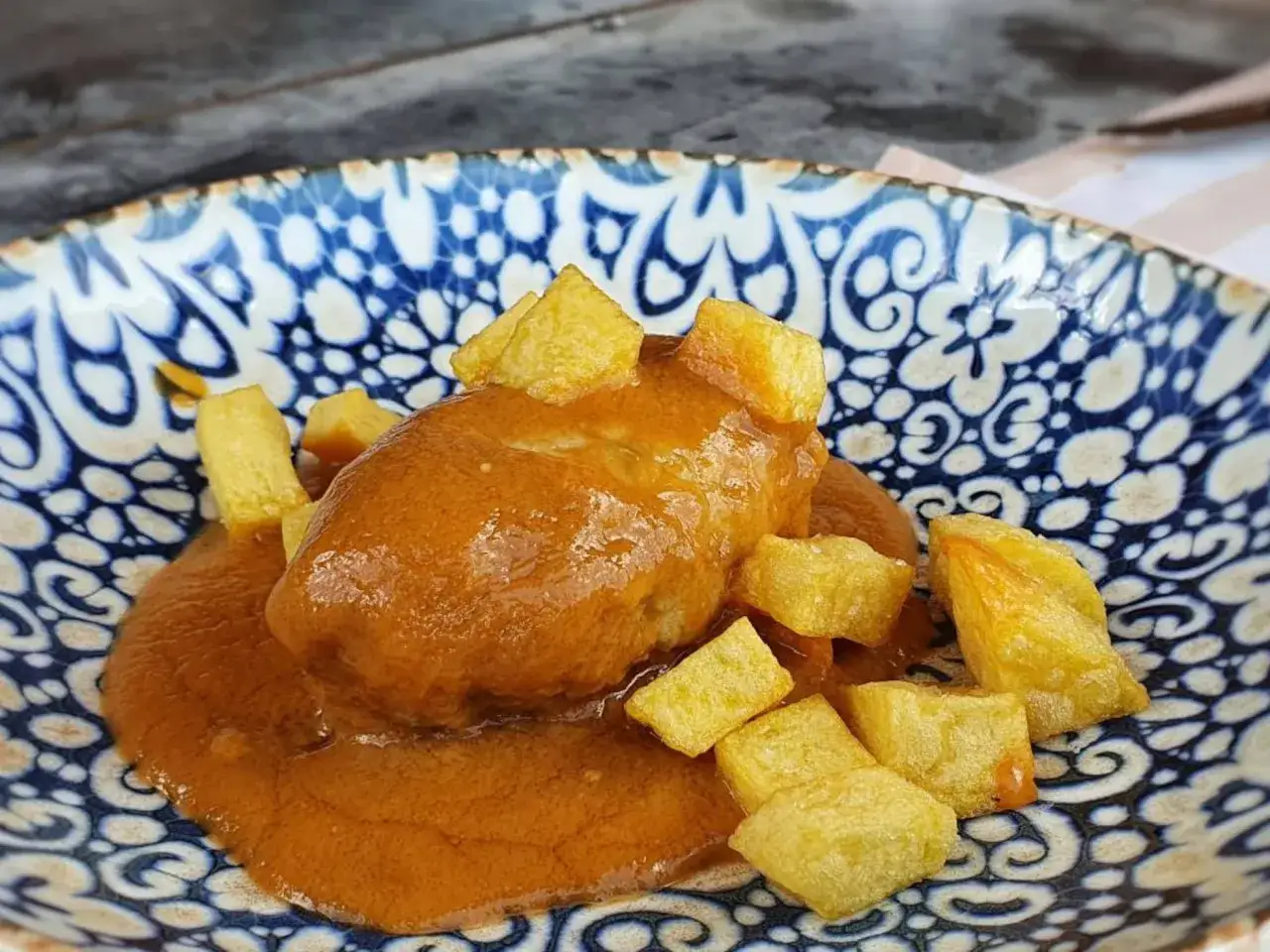 Rollo de bonito en salsa con patatas fritas, servido en un plato azul y blanco.