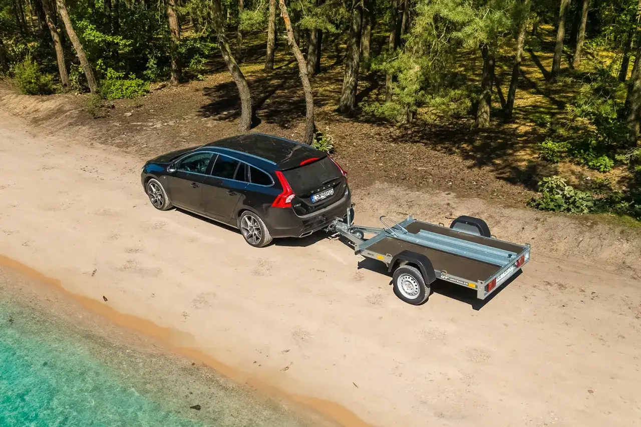 Czarne Volvo z przyczepą na piaskowej drodze w lesie, obok wody. Manewrowanie z przyczepą wymaga wprawy.