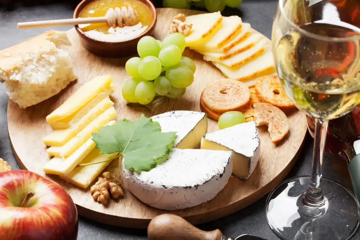 En ostbricka med brieost, vindruvor, honung, kex och ett glas vitt vin. Perfekt för en mysig kväll med vin till brieost.