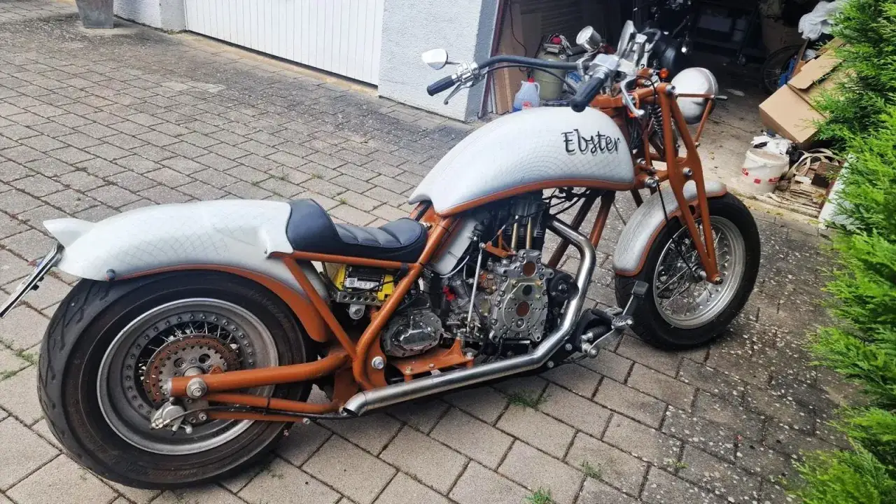Customizada moto diesel con tanque blanco y detalles naranjas, lista para la carretera.