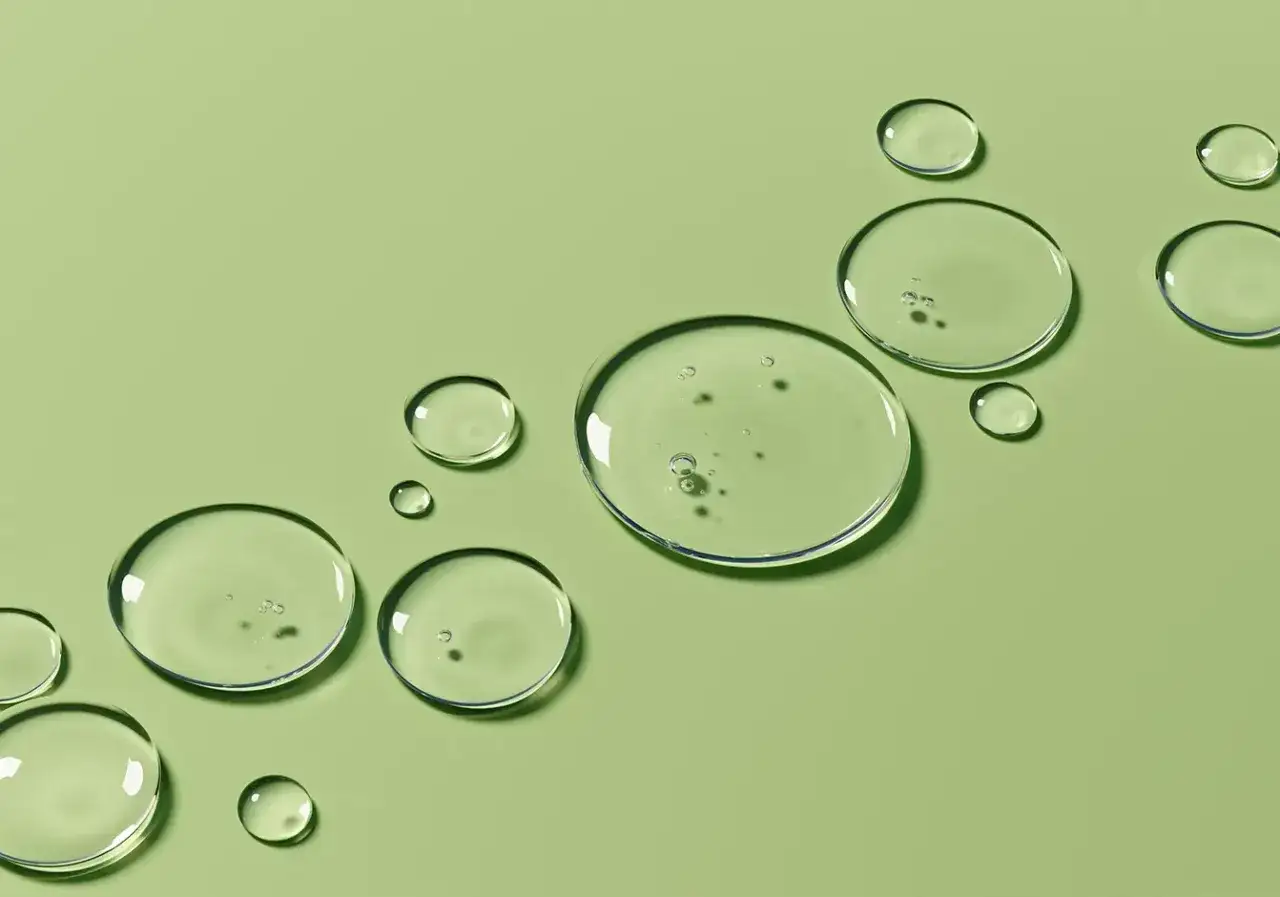 Klare Tropfen auf grünem Hintergrund, die an die sanfte vitamin e haut auftragen erinnern.