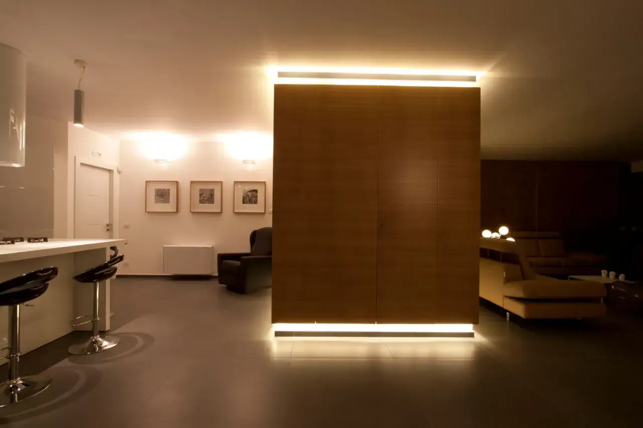 Un elegante divisorio in cartongesso, rivestito in legno, illumina con luce soffusa creando un'atmosfera accogliente.
