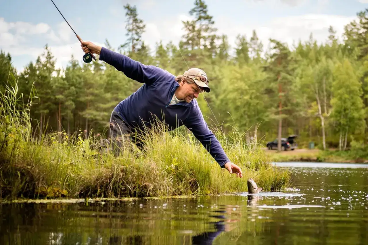 Man med fiskeutrustning lyckas f&aring;nga en fisk vid en sj&ouml; i &Aring;nnaboda.