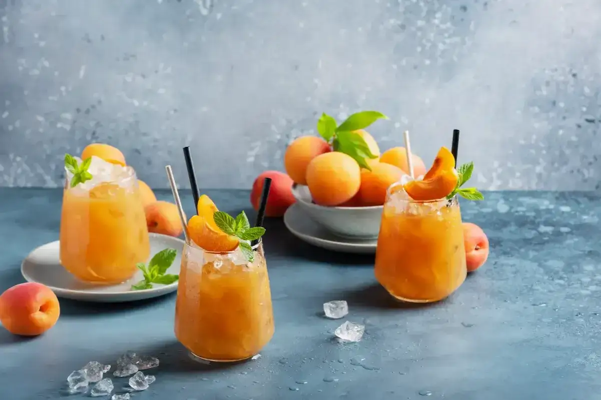 Trois cocktails rafra&icirc;chissants au jus d'abricot alcool, garnis de menthe et de quartiers d'abricot, sur un fond bleu textur&eacute;.