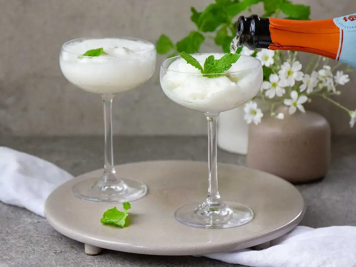 Två frostiga Hugo Spritz-drinkar med mynta, en flaska mousserande vin hälls i.