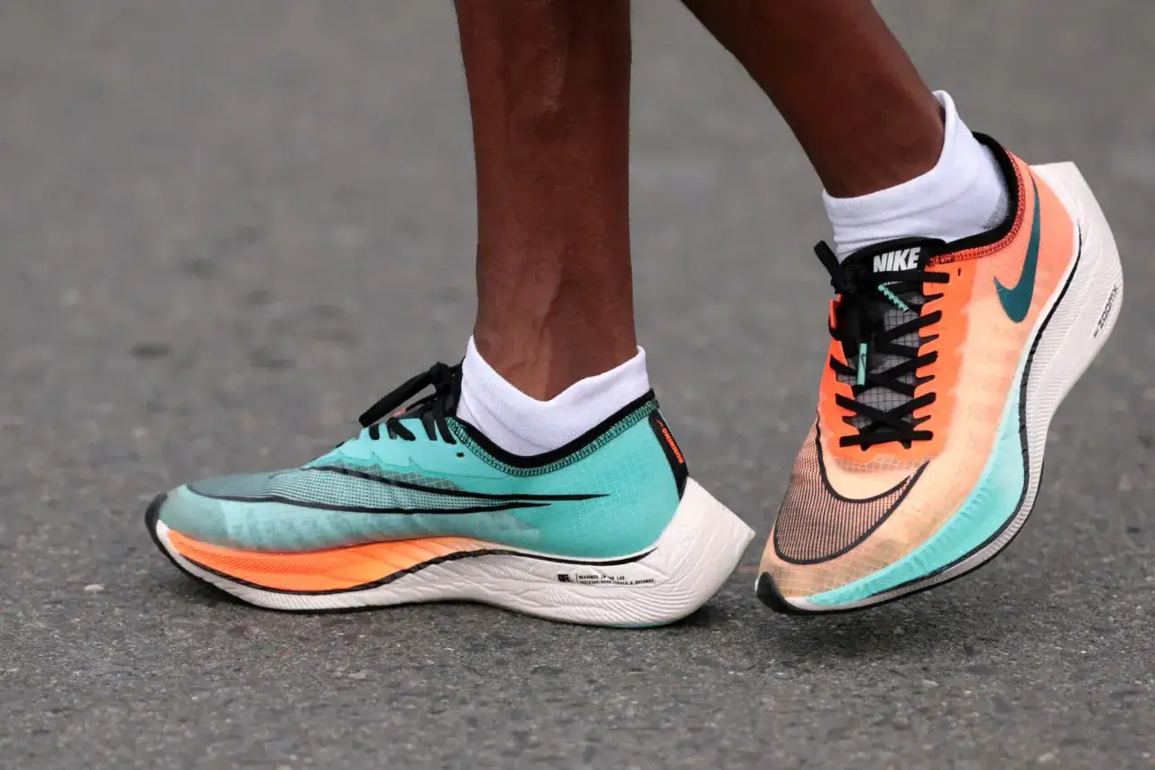 Biegacz w turkusowo-pomarańczowych butach Nike z dużą amortyzacją, gotowy na pokonywanie kilometrów.
