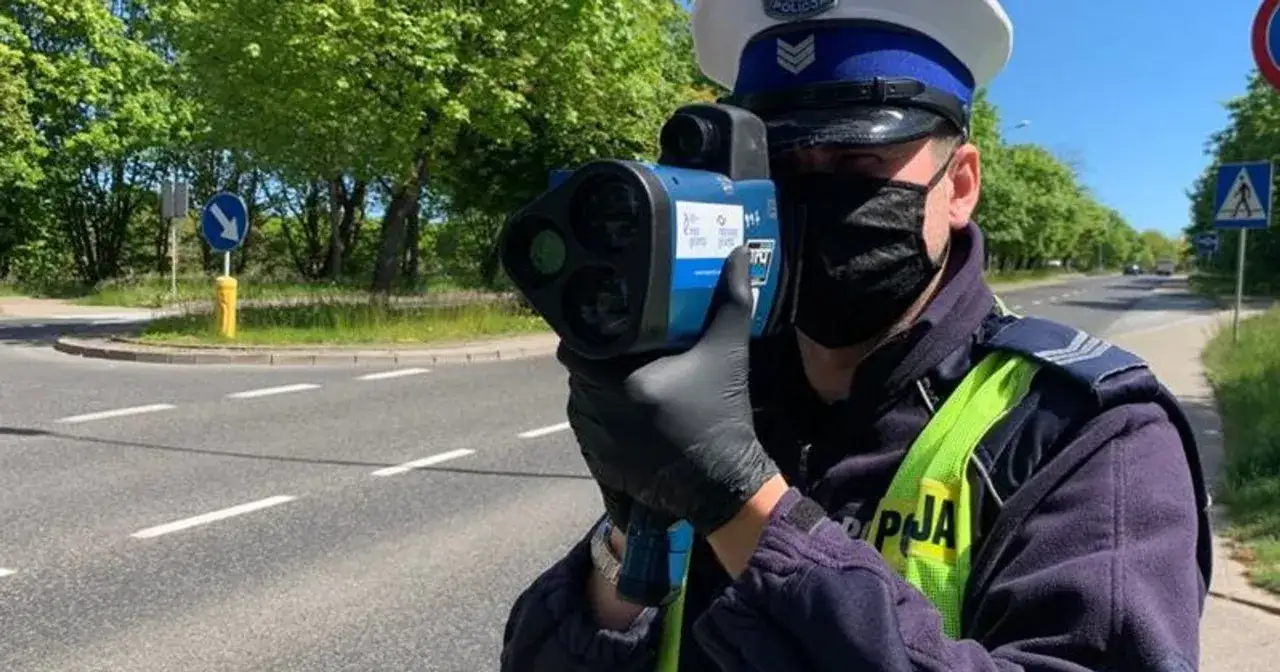 Policjant w masce i rękawiczkach wykonuje radarowy pomiar prędkości na drodze.