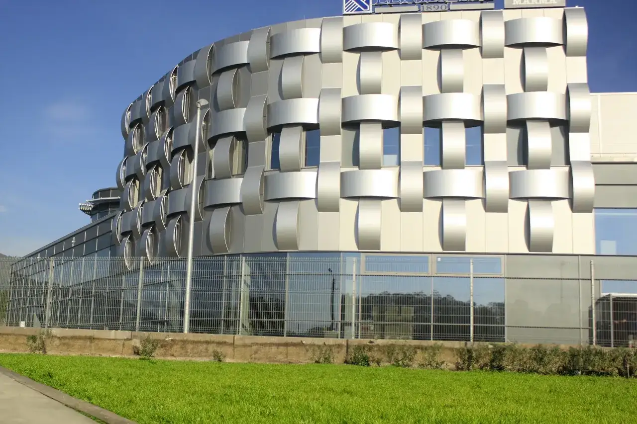 Nowoczesny budynek z fasadą z **alucobondu** o geometrycznym wzorze, odbijający niebo i zieleń.