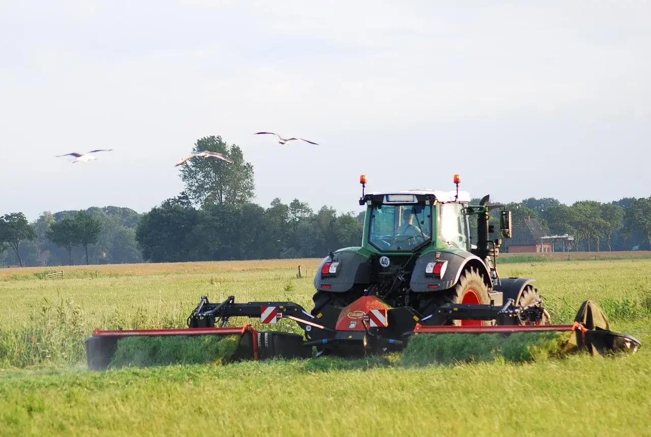 Zielony traktor z zamontowanym dyskiem koszącym, który jest napędzany przez wałek przekazu mocy, pracuje na zielonym polu.