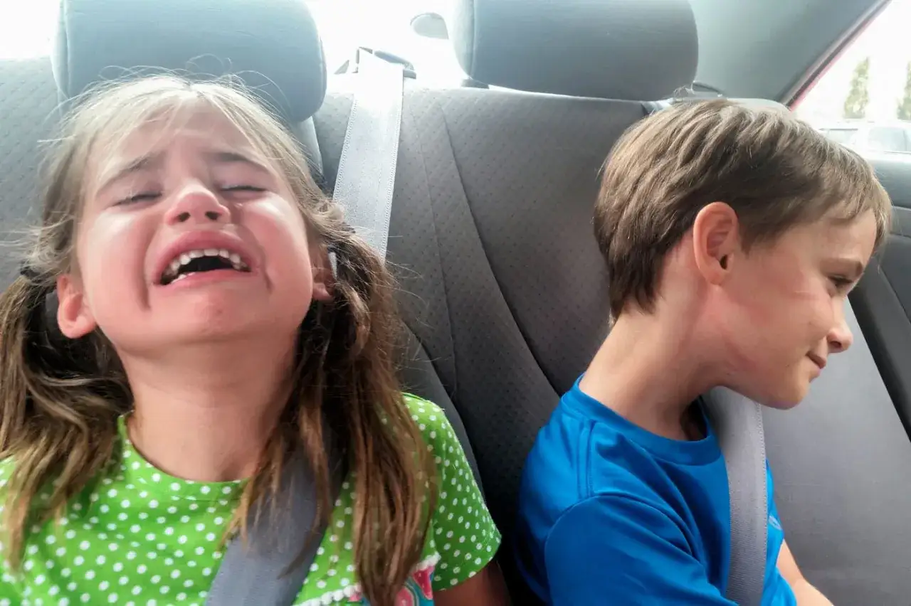 Ni&ntilde;a llorando en el asiento trasero del coche, mientras su hermano, mi hijo de 9 a&ntilde;os, se enoja por todo y mira hacia otro lado.