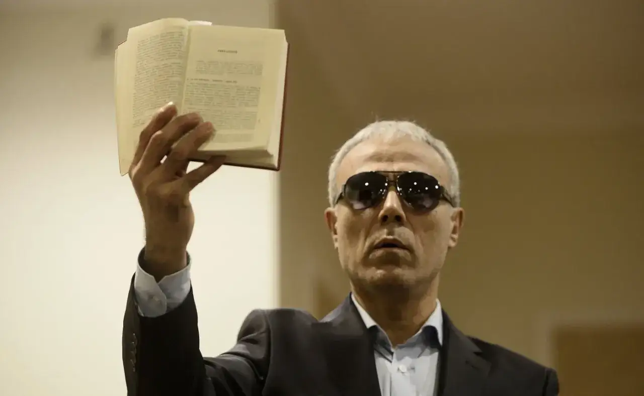 Ali Agca dzisiaj, w okularach przeciwsłonecznych, trzyma otwartą książkę.