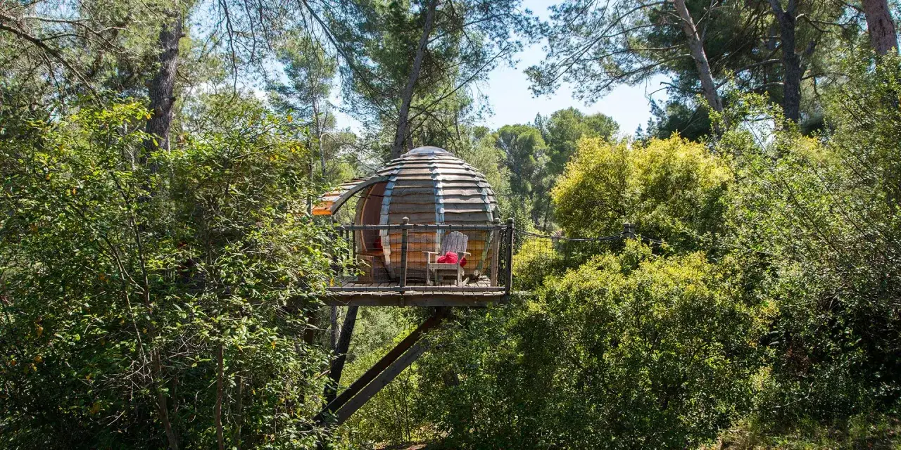 Cabane ronde perchée, idéale pour un glamping paca. Un fauteuil invitant sur la terrasse boisée.
