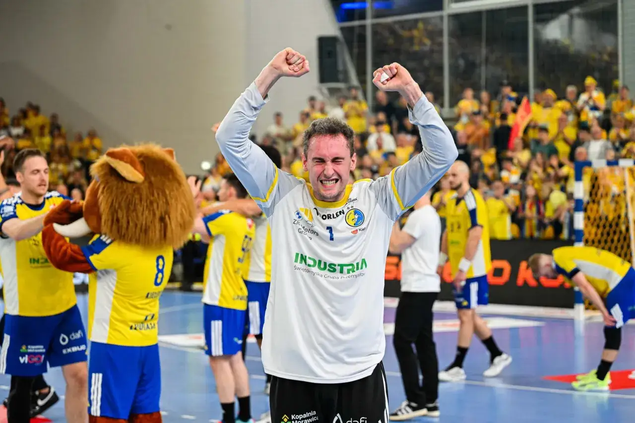 Adam Morawski świętuje zwycięstwo z drużyną, otoczony przez kolegów i maskotkę.
