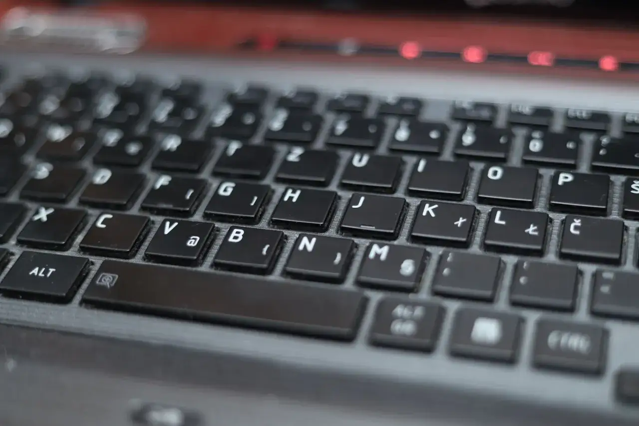 Zbliżenie na klawiaturę laptopa, widoczne klawisze z literami i symbolami, gotowe do wprowadzania tekstu.