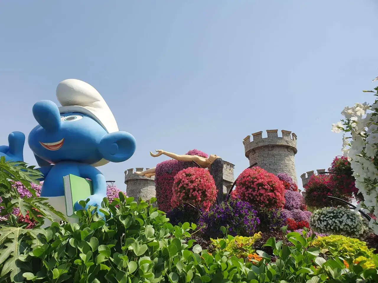 Smerf z książką wita w Miracle Garden w Dubaju, gdzie kwitnące zamki i rzeźby tworzą bajkowy świat.