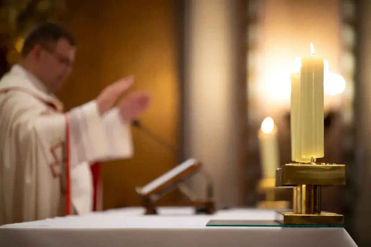 Ksiądz w białej szacie błogosławi wiernych. Płoną świece, symbolizując pierwszy dzień tygodnia w kościele katolickim.