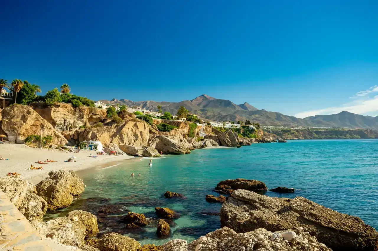 Aguas cristalinas y arena dorada en las **Nerja beaches**, con acantilados y montañas al fondo. Un paraíso para relajarse.