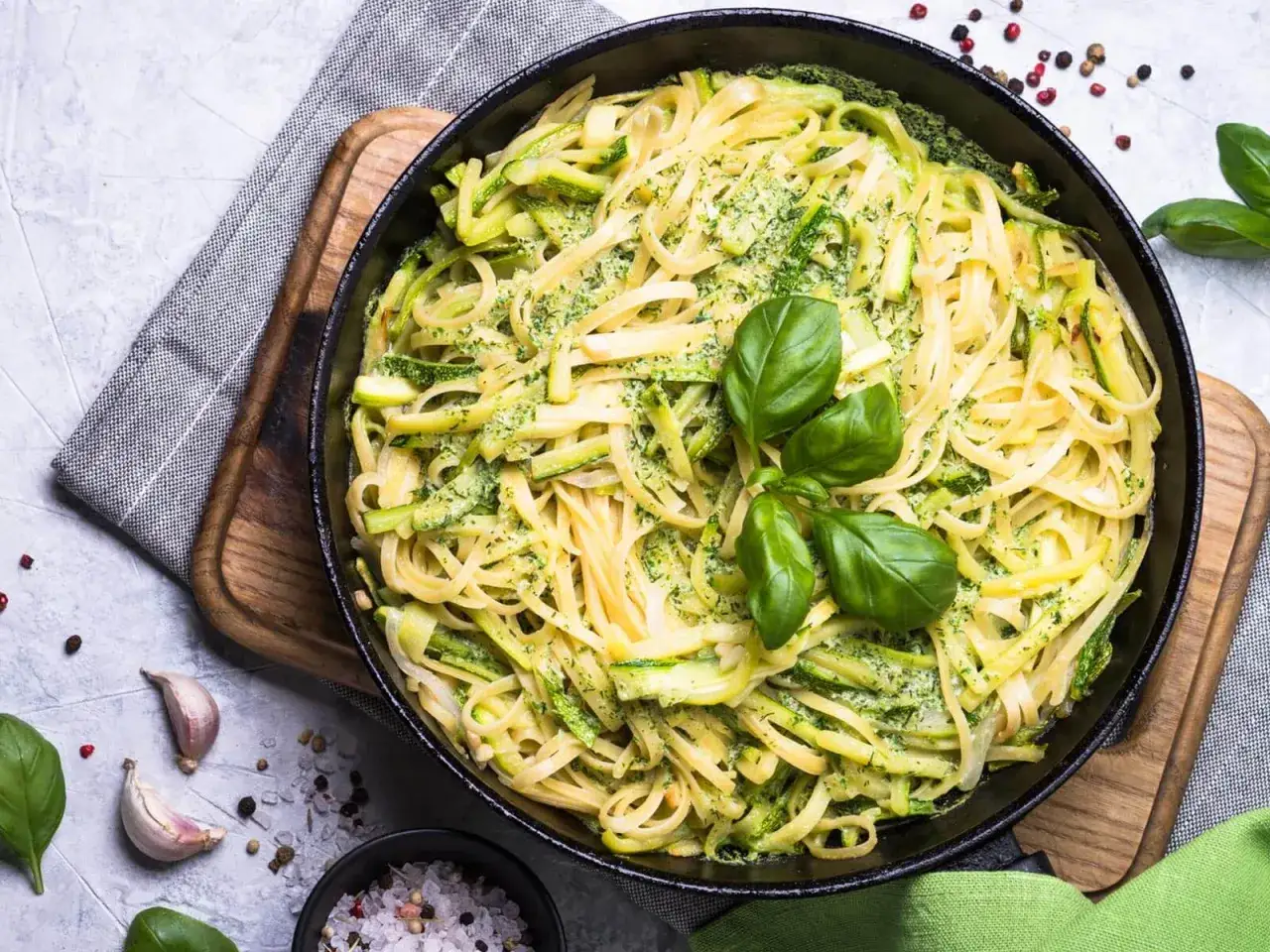 Cremige Nudelgerichte mit Zucchini und frischem Basilikum in einer Pfanne, garniert mit Knoblauch und Gew&uuml;rzen.