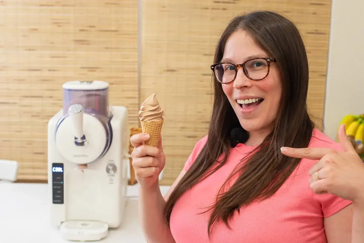 Frau hält Schokoeis-Tüte, daneben eine Eismaschine. Perfekt für ein schnelles Schokoeis Rezept mit Eismaschine.