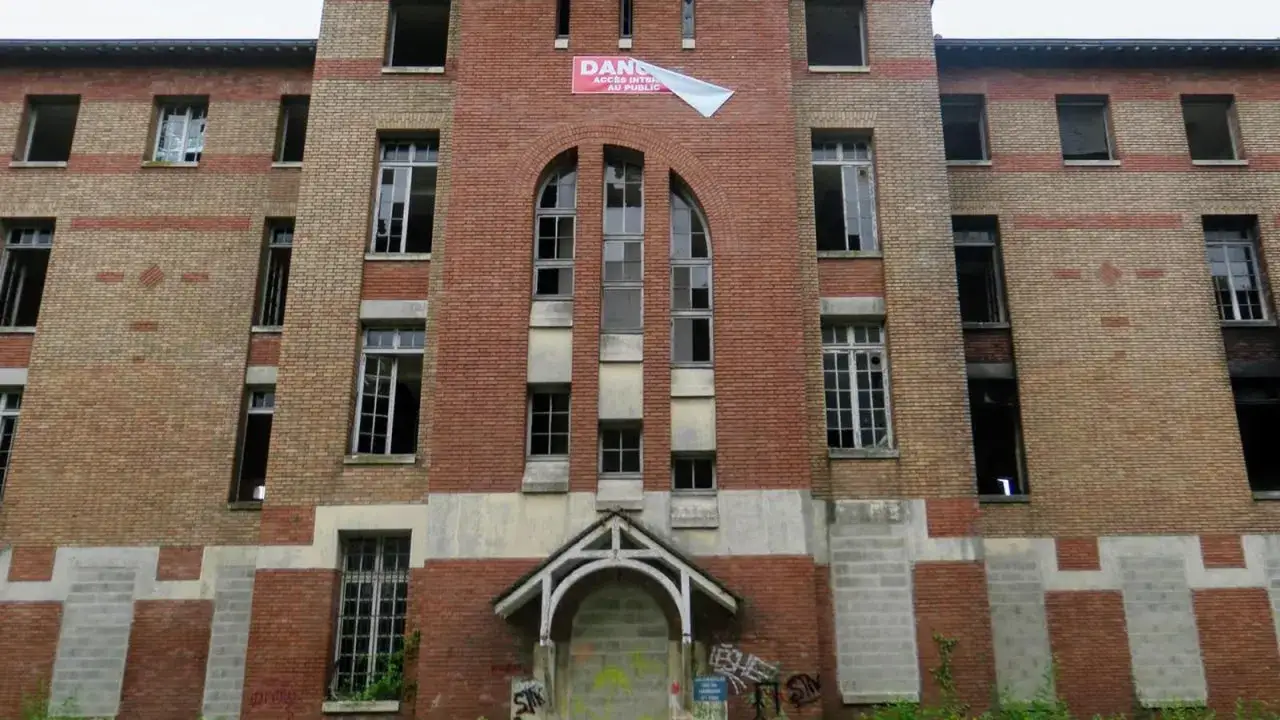 Fa&ccedil;ade de l'h&ocirc;pital abandonn&eacute; d'Angicourt, avec ses fen&ecirc;tres bris&eacute;es et un panneau 