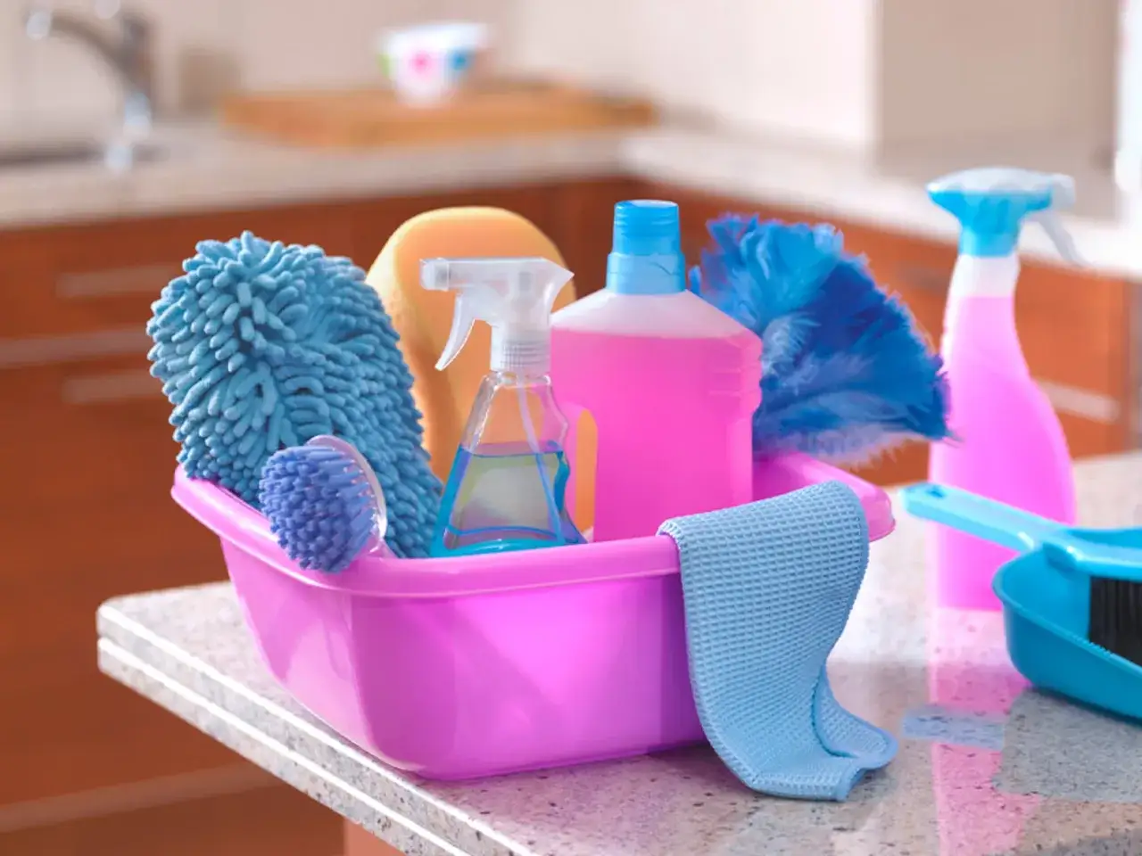 Cesta rosa con 25 productos de limpieza del hogar: esponja, cepillo, plumeros, botellas de spray y pa&ntilde;o.