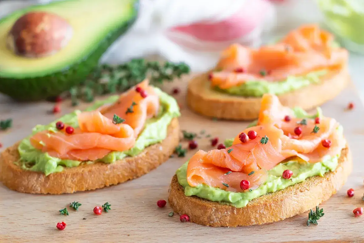 Bruschette con salmone affumicato e crema di avocado, guarnite con pepe rosa e timo. Un'esplosione di freschezza e sapore.