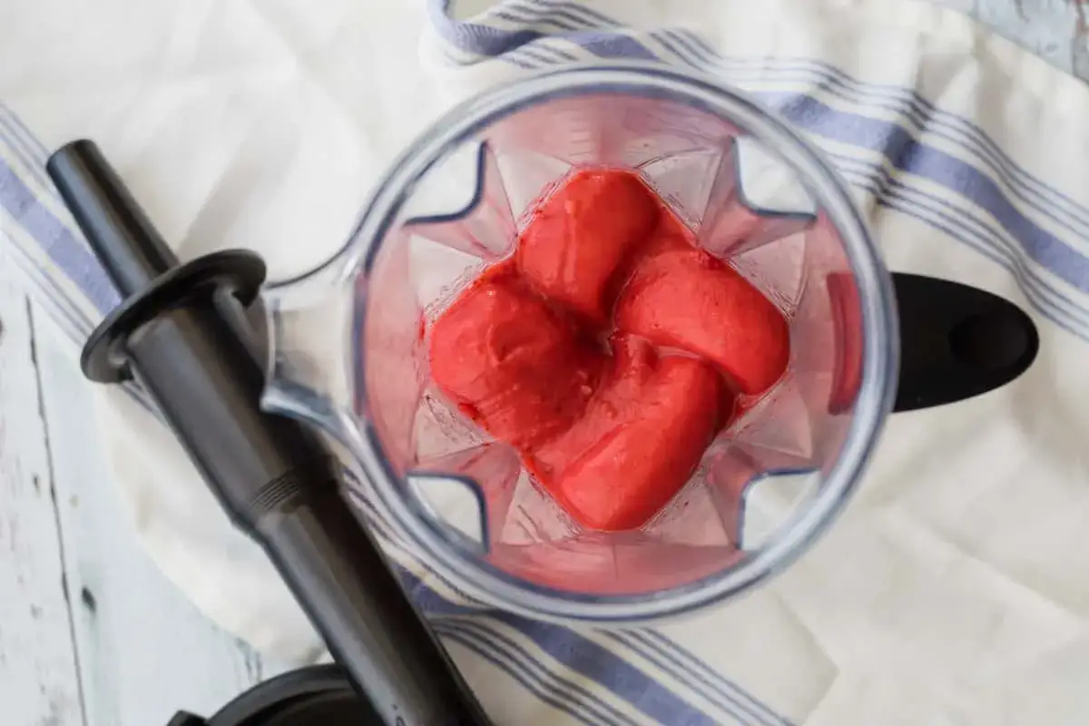 Gros morceaux de fraises congelées dans un mixeur, prêts pour une recette de purée de fraise maison.