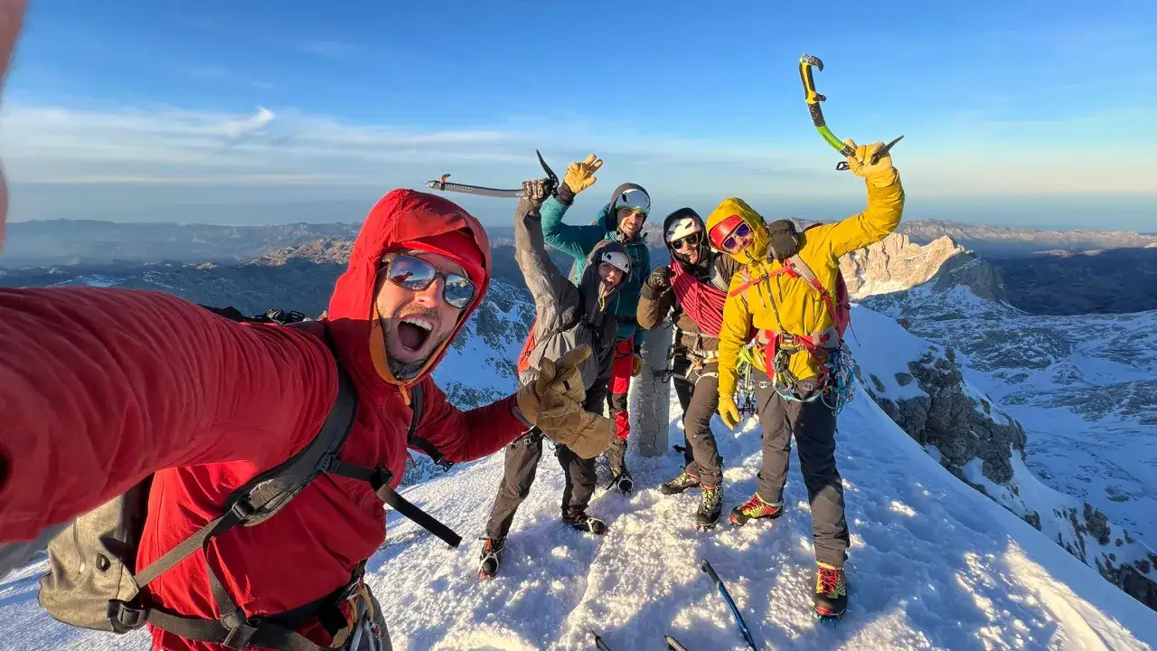 Grupo de montañistas celebra en la cima nevada tras exitosas excursiones nieve. Llevan equipo de escalada y piolet.