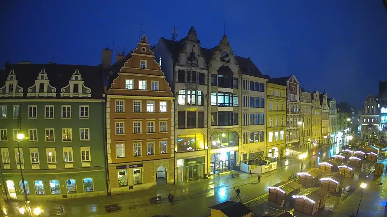 Kolorowe kamienice na wrocławskim Rynku nocą, oświetlone latarniami i jarmarkowymi budkami.