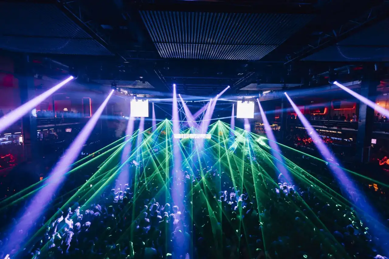 Una multitud baila bajo luces l&aacute;ser verdes y moradas en una discoteca. El evento, con el c&oacute;digo 11 octubre, crea una atm&oacute;sfera vibrante.