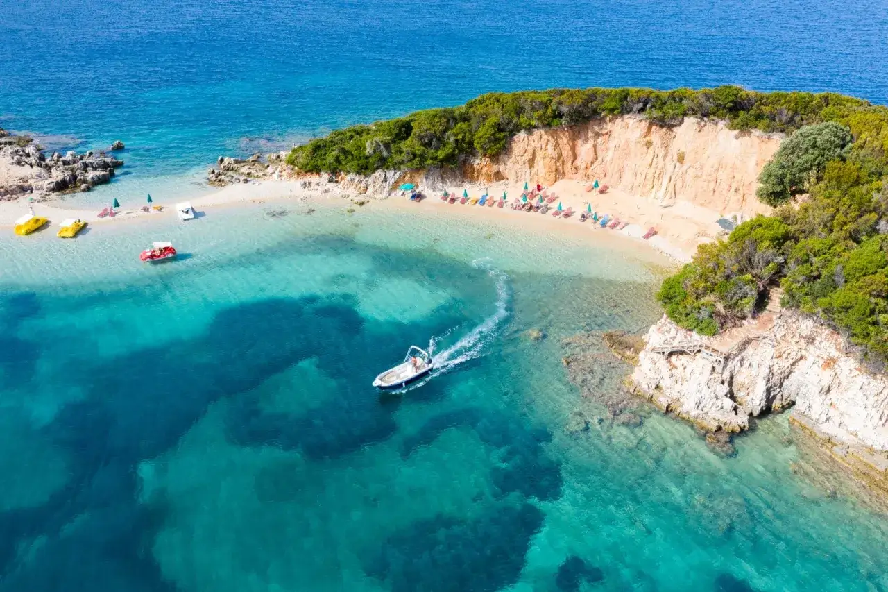 Rajska plaża na riwierze albańskiej z łódką na turkusowej wodzie i leżakami na piasku.