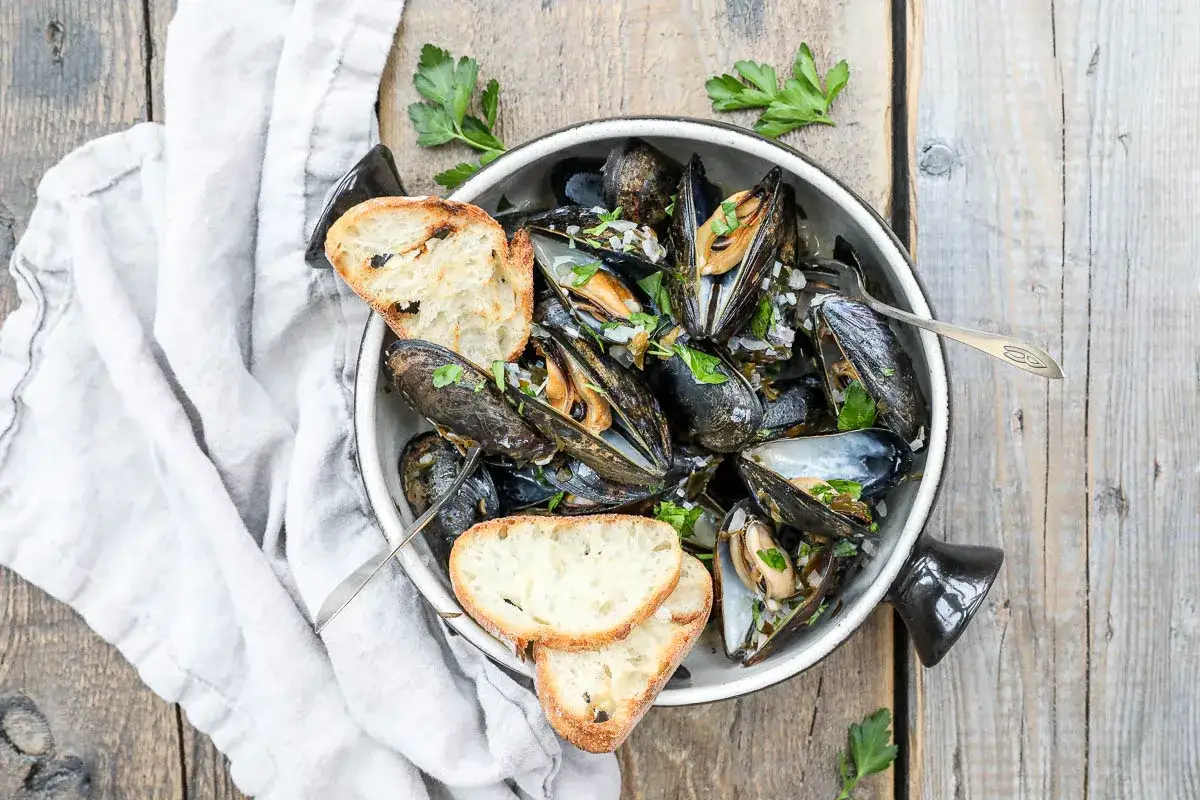 En sk&aring;l med &aring;ngade moules marini&egrave;res, toppad med persilja och serverad med rostat br&ouml;d.