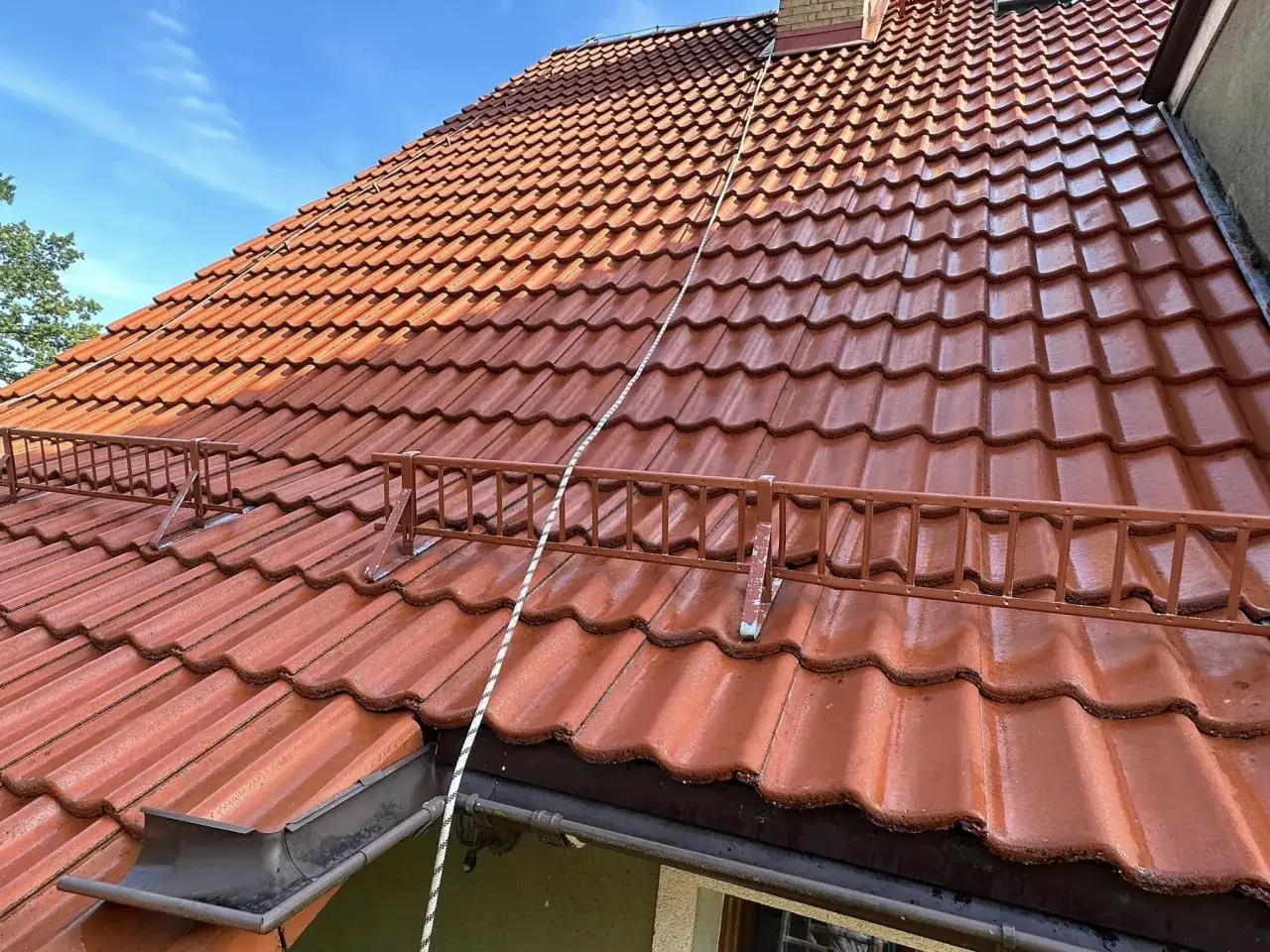 Czerwony dach z gontów bitumicznych, na którym widać ślady po mchu. Dowiedz się, jak usunąć mech z gontów bitumicznych, by dach znów lśnił.