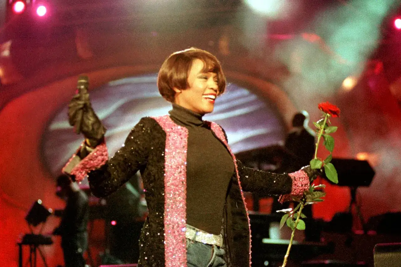 Whitney Houston w Polsce, na scenie z mikrofonem i czerwoną różą, w błyszczącej marynarce.
