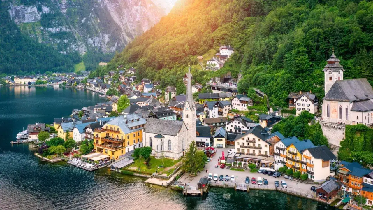 Malownicze jeziora w Austrii, z urokliwą wioską Hallstatt u podnóża gór. Słońce oświetla zielone zbocza i zabytkowe budynki.