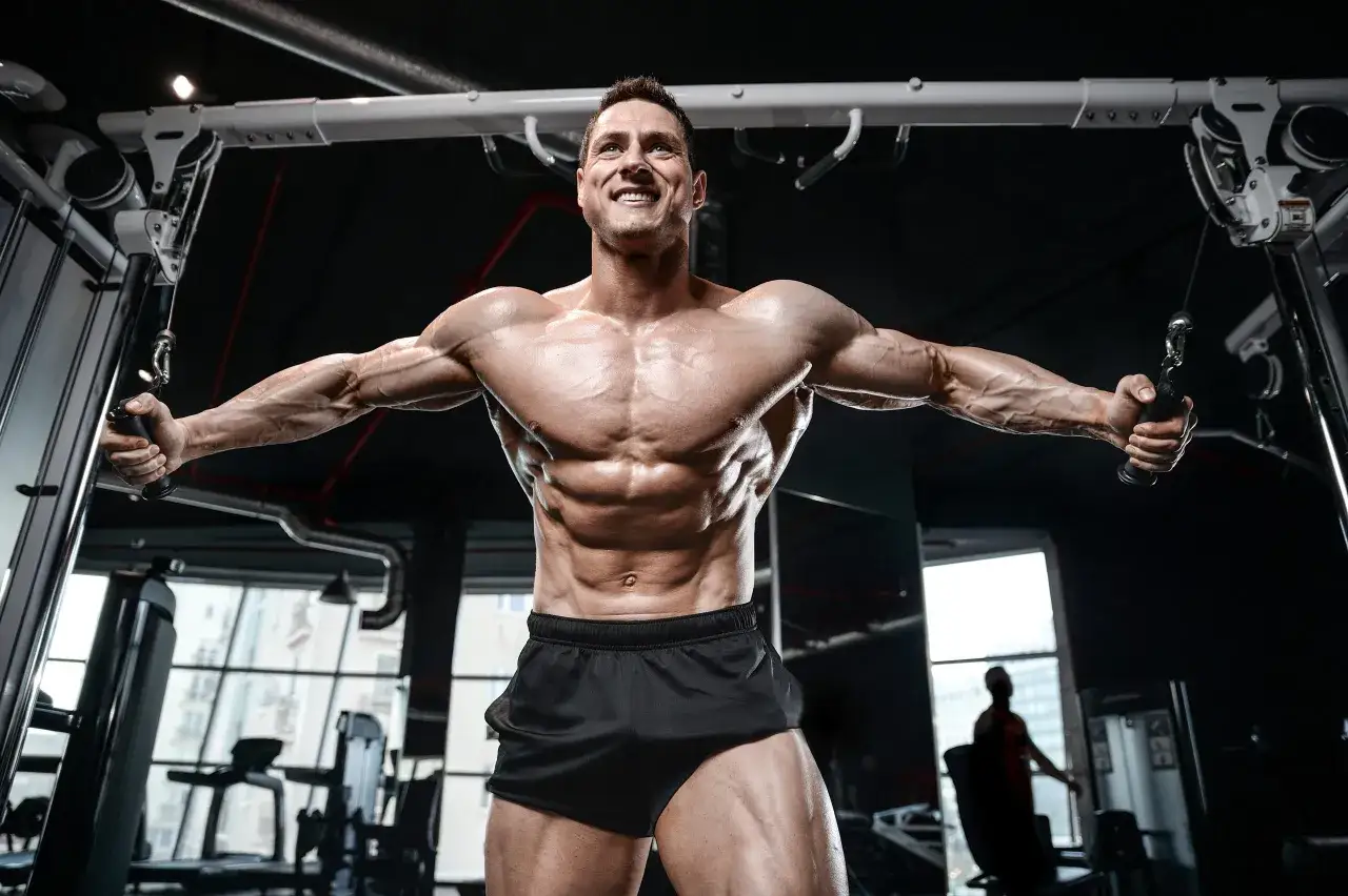 Uśmiechnięty mężczyzna wykonuje trening klatka barki na maszynie typu cable cross.