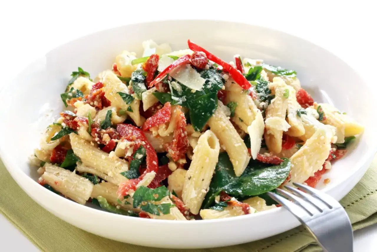 Ein köstlicher nudelsalat mit getrockneten tomaten, garniert mit Parmesan und frischer Petersilie, serviert in einer weißen Schüssel.
