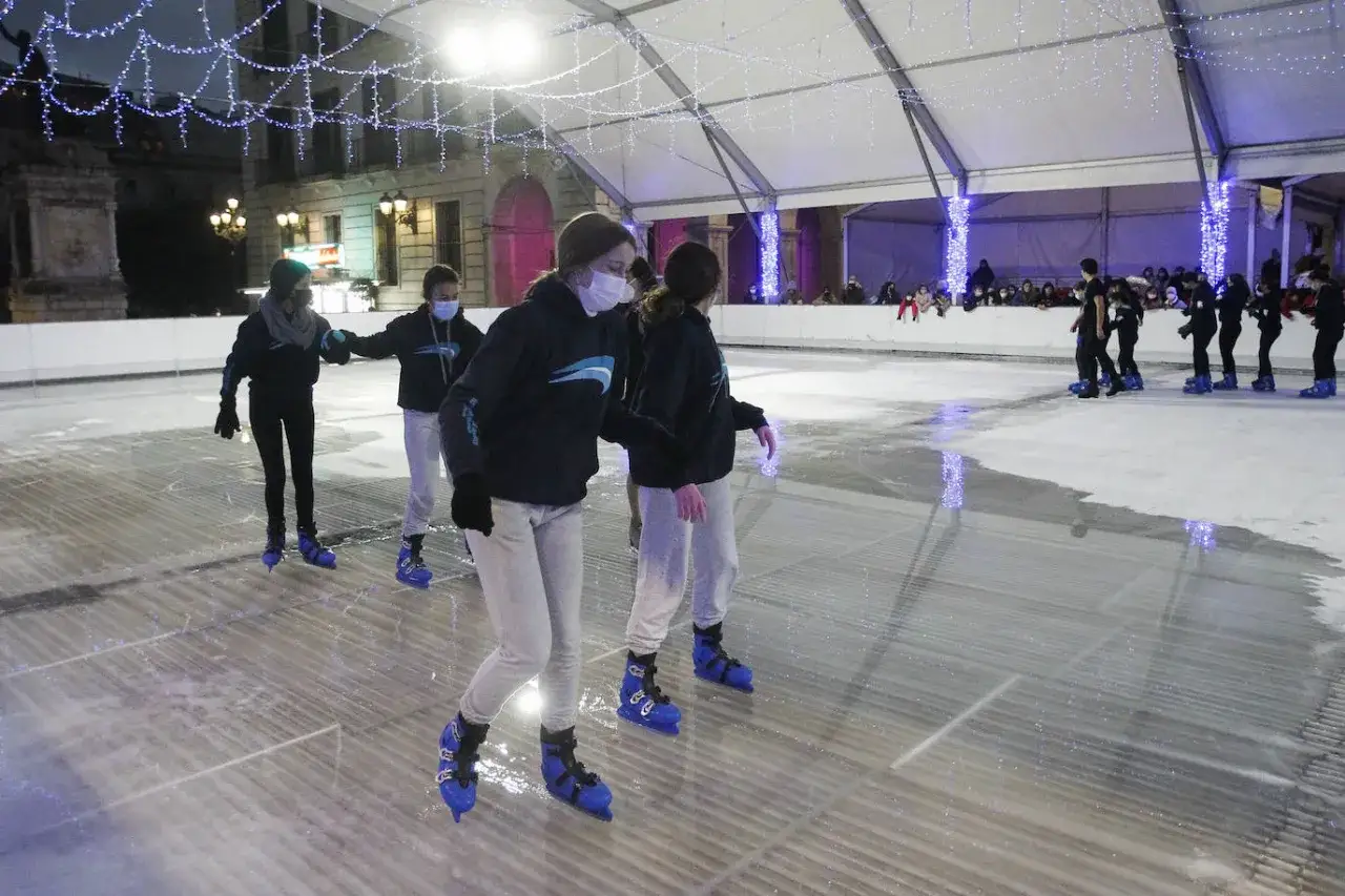 Ni&ntilde;os patinan en la pista de hielo Santander, bajo luces festivas.