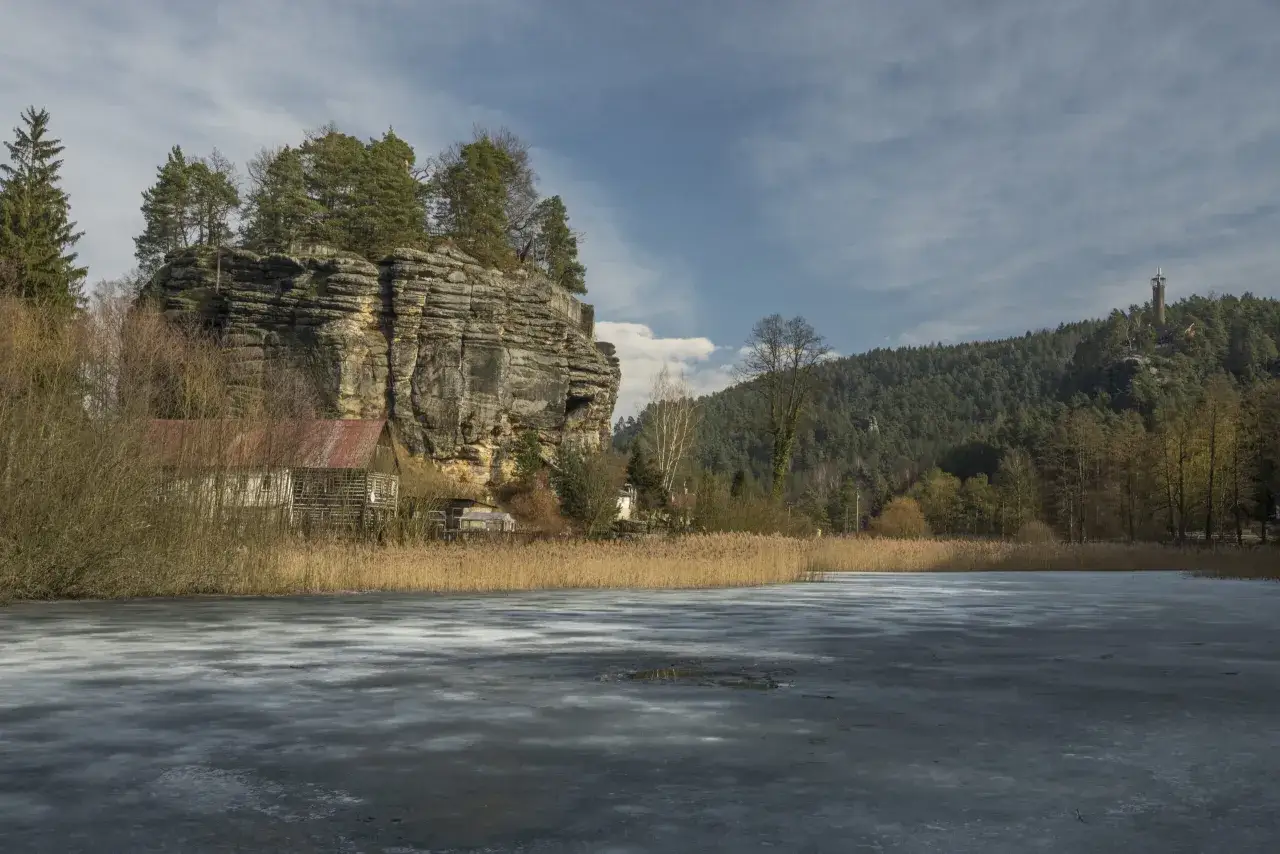 Einsiedlerstein: eine Felsenburg thront &uuml;ber einem zugefrorenen Teich, umgeben von Schilf und B&auml;umen.