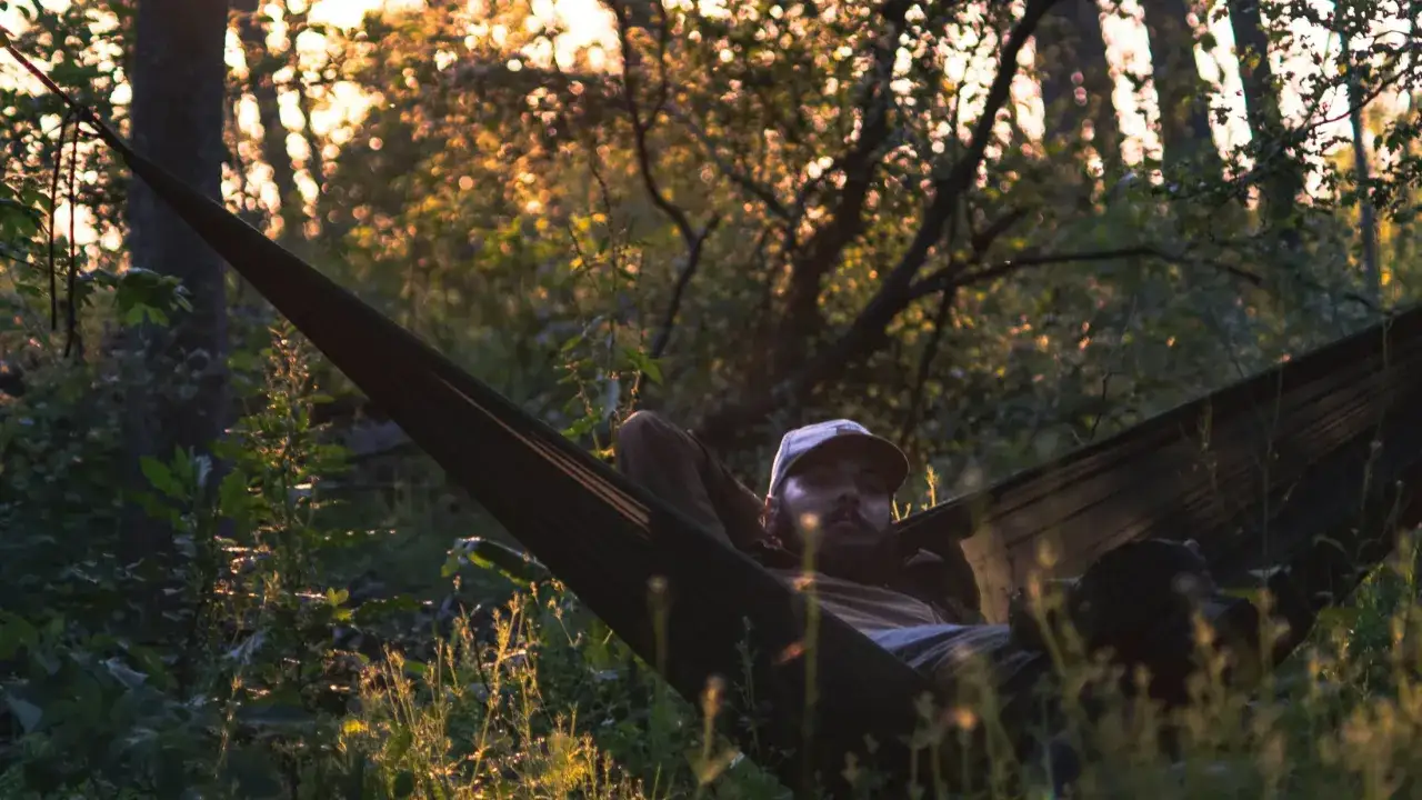 Hombre descansando en hamaca durante acampada libre en Cantabria. El sol se filtra entre los árboles creando un ambiente mágico.