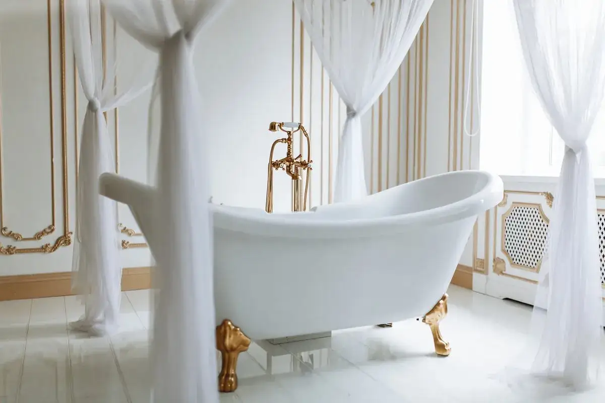 Baignoire &icirc;lot blanche sur pieds dor&eacute;s, robinetterie vintage. Un guide pour comment fixer une baignoire dans une salle de bain luxueuse.