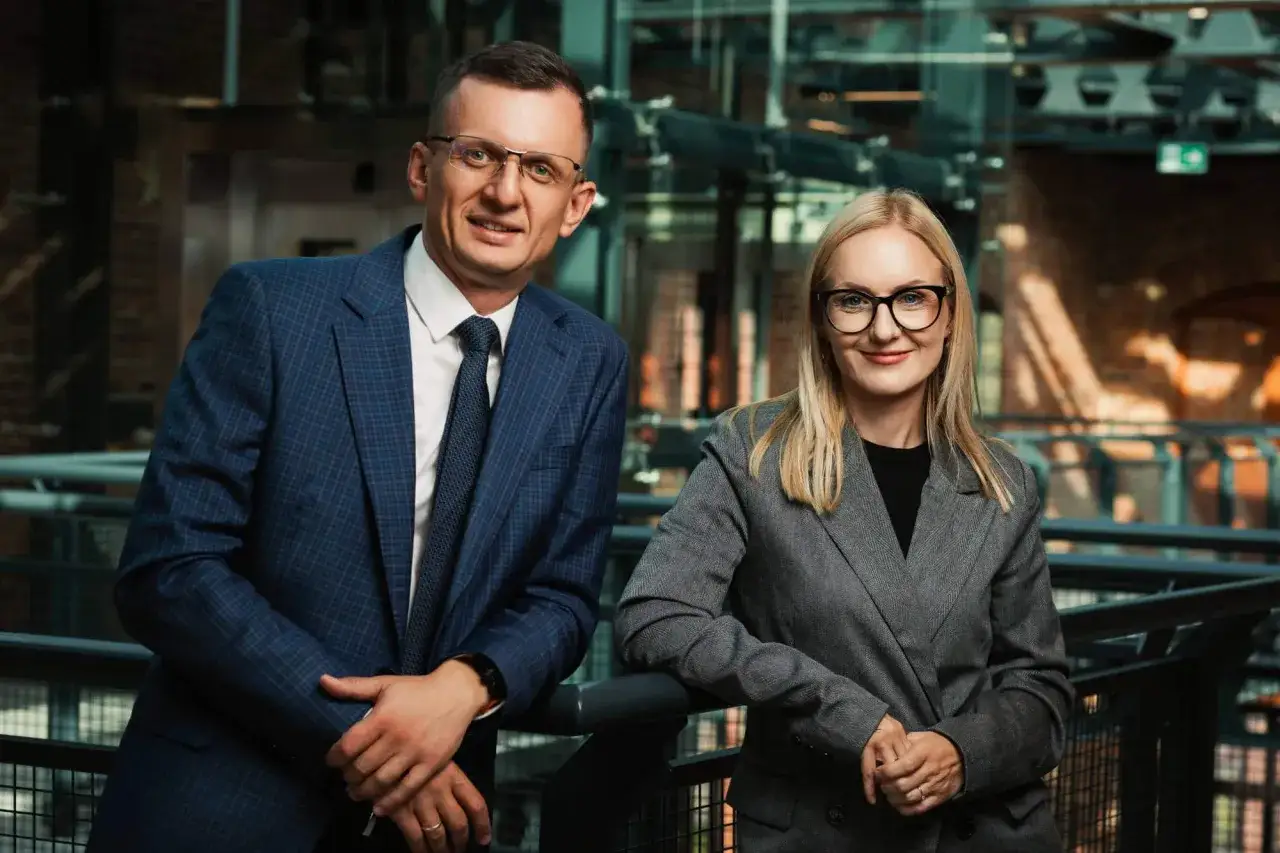 Para w garniturach, mężczyzna i kobieta, pozuje na tle nowoczesnego wnętrza.